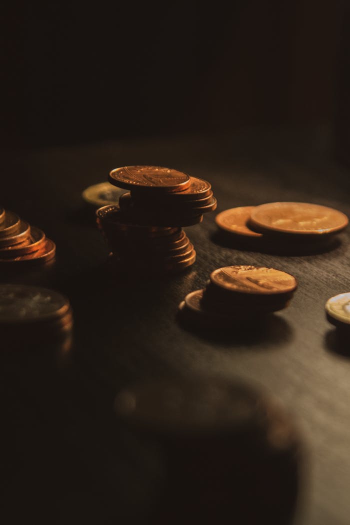 Close-up of a stack of bronze coins on a wooden surface in dim lighting.